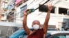 FILE - A Buddhist monk flashes the three-fingered salute of resistance while holding a smartphone as he watches protesters march in Yangon, Myanmar, Feb. 7, 2021. 