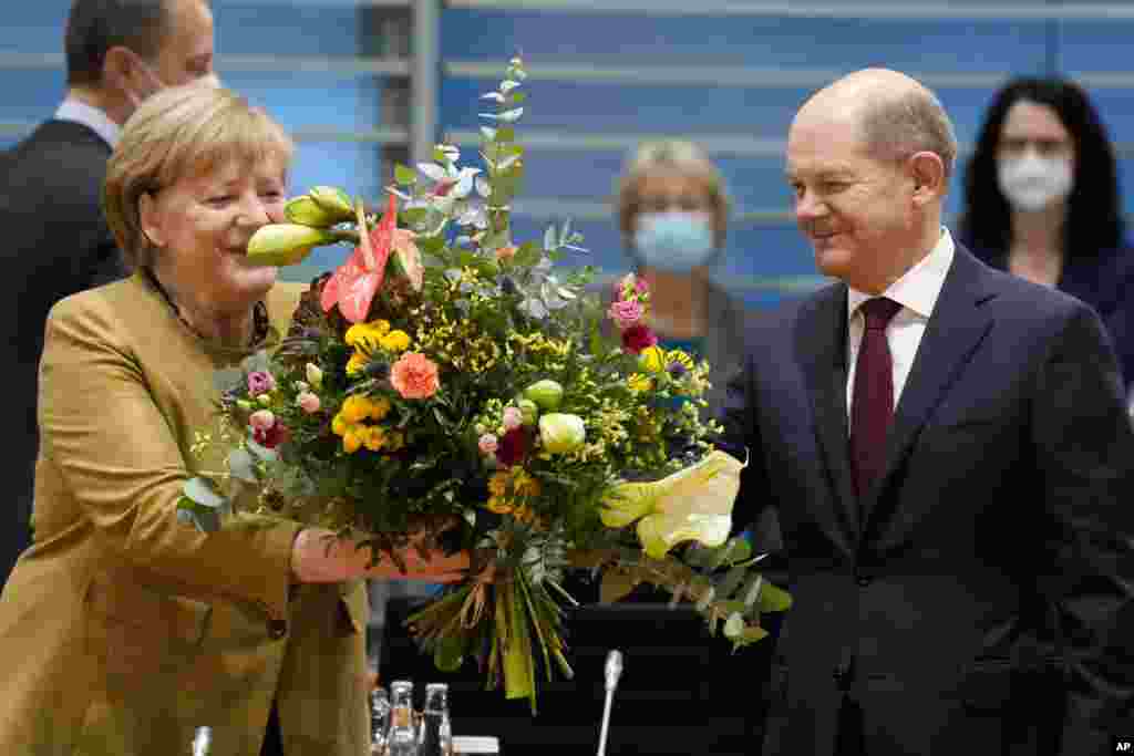 German Chancellor Angela Merkel, left, receives a bouquet from Vice Chancellor and Finance Minister Olaf, Scholz, right, prior to the cabinet meeting at the chancellery in Berlin, Germany, Nov. 24, 2021.