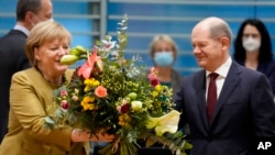 German Chancellor Angela Merkel, left, receives a bouquet from Vice Chancellor and Finance Minister Olaf, Scholz, right, prior to the cabinet meeting at the chancellery in Berlin, Germany, Nov. 24, 2021.