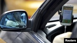 FILE - A taxi driver is reflected in a side mirror as he uses the Didi Chuxing car-hailing application in Beijing, China, Sept. 22, 2015. 