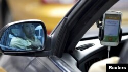 FILE - A taxi driver is reflected in a side mirror as he uses the Didi Chuxing car-hailing application in Beijing, China, Sept. 22, 2015. 