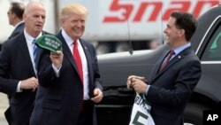 FILE - Wisconsin Gov. Scott Walker, right, presents President Donald Trump with a Milwaukee Buck basketball hat and jersey as he arrives in Kenosha, Wisconsin, April 18, 2017. The ceremonial groundbreaking for a massive $10 billion Foxconn factory complex in Wisconsin was supposed to be evidence that the manufacturing revival fueled by Trump's "America First" policy is well underway. But an announcement this week by Harley-Davidson that it is moving some production of motorcycles overseas to avoid tariffs is fueling unease among voters in Wisconsin, a state Trump barely won and where fellow Republican Gov. Scott Walker is on the ballot.
