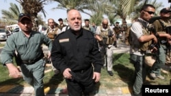 FILE - Iraq's Prime Minister Haider al-Abadi (in black) walks during a visit to an Iraqi army base in Camp Tariq near Fallujah, Iraq, June 1, 2016. Abadi is calling on residents of Mosul to cooperate with government forces that will be participating in operations to retake the city from IS militants.
