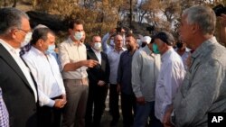 In this photo released Oct. 13, 2020 on the official Facebook page of the Syrian Presidency, Syrian President Bashar Assad, third from left, wearing a mask speaks with people during his visit to assess damage in last week’s deadly wildfires.