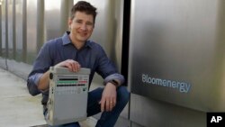 Joe Tavi, Bloom Energy senior director of manufacturing, holds a refurbished ventilator as he kneels beside fuel cells, Wednesday, April 1, 2020, in Sunnyvale, Calif. The new coronavirus outbreak has prompted companies large and small to rethink how…