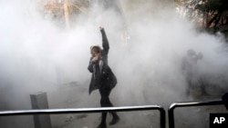 A university student attends a protest at Tehran University while a smoke grenade is thrown by anti-riot police, in Tehran, Iran, Dec. 30, 2017. A wave of spontaneous protests over Iran's weak economy swept into Tehran Saturday, with college students and others chanting against the government hours after hard-liners rallied in support of the clerical establishment.