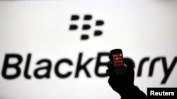 A man silhouetted against a video screen with the Blackberry logo poses with a Blackberry Q10, September 21, 2013.