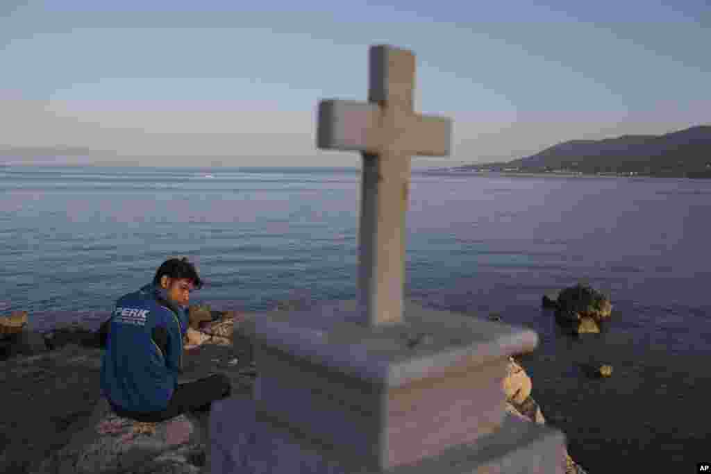A Pakistani migrant stranded on the Greek island of Lesbos sits behind a cross near the port of Mytilini. Pope Francis will visit the island Saturday joined by Ecumenical Patriarch Bartholomew and the head of the Orthodox Church of Greece, Athens Archbishop Ieronymos II.