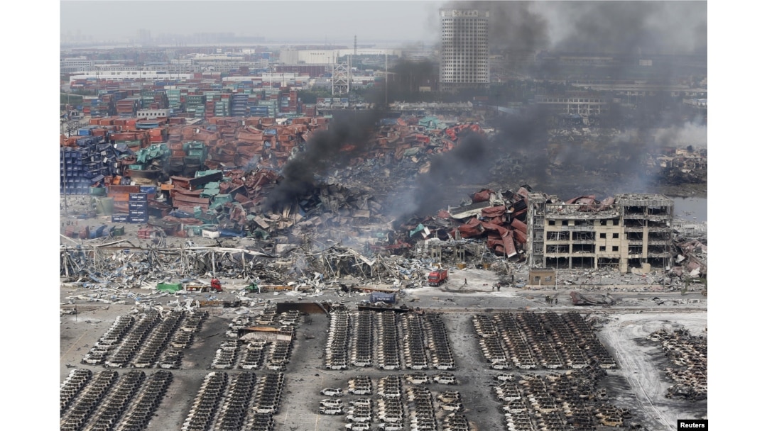Smoke rises among shipping containers next to damaged vehicles as firefighters try to put out a fire after explosions on Wednesday night, at Binhai new district in Tianjin, China, Aug. 14, 2015.