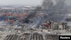 Smoke rises among shipping containers next to damaged vehicles as firefighters try to put out a fire after explosions on Wednesday night, at Binhai new district in Tianjin, China, Aug. 14, 2015.