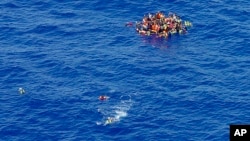 FILE - Migrants swim while others climbed onto a rescue dinghy to wait for rescuers on the scene of the capsizing and sinking of a fishing boat in the Mediterranean sea off Libya. 