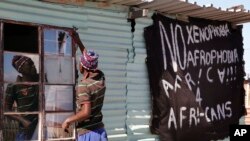 Un homme répare une vitre brisée à côté d'une banderole où l'on peut lire : "Non à la xénophobie et àl' afrophobie" à Philippi dans la banlieue du Cap, en Afrique du Sud, le 20 avril 2015.