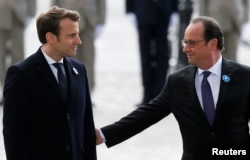 Outgoing French President Francois Hollande (R) reaches out to touch President-elect Emmanuel Macron, as they attend a ceremony to mark the end of World War II at the Tomb of the Unknown Soldier at the Arc de Triomphe in Paris, May 8, 2017.