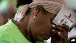 FILE - Marie Jean-Louis bows her head as she holds her Employment Authorization card and photographs of her family in Haiti during a vigil sponsored by Haitian Women of Miami at the Notre Dame Catholic Church in the Little Haiti neighborhood of Miami.