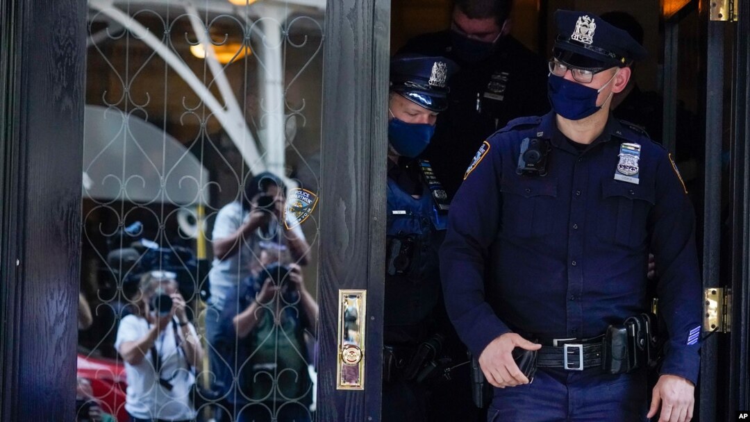 New York City police officers walk out of the apartment building where former New York Mayor Rudy Giuliani resides as members of the media observe, April 28, 2021.