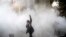 A university student attends a protest inside Tehran University while a smoke grenade is thrown by anti-riot Iranian police, in Tehran, Iran, Dec. 30, 2017. A wave of spontaneous protests over Iran's weak economy swept into Tehran Saturday, with college 