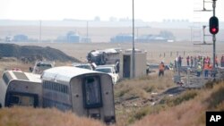 Workers stand near train tracks, Sept. 27, 2021, next to overturned cars from an Amtrak train that derailed Saturday, near Joplin, Mont., killing three people and injuring others.