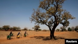 FILE - Girls carry water on their bicycles at a dispensary in Nedogo village near Ouagadougou, Burkina Faso, Feb. 16, 2018.