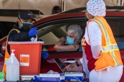 FILE - FILE - A woman is vaccinated inside her vehicle at a mass COVID-19 vaccination site outside The Forum in Inglewood, Calif., Jan. 26, 2021.