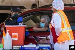 FILE - FILE - A woman is vaccinated inside her vehicle at a mass COVID-19 vaccination site outside The Forum in Inglewood, Calif., Jan. 26, 2021.