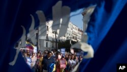 Seen through a hole in a torn Venezuelan flag, people gather to protest in support of families and friends in Venezuela during a protest in Madrid, Spain, April 19, 2017. Opponents of Venezuelan President Nicolas Maduro called on people to take to the streets and march against the embattled socialist leader. 