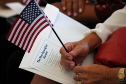 FILE - A soon-to-be U.S. citizen holds an American flag and a card with the words to The Star Spangled Banner before the start of a naturalization ceremony at an U.S. Citizenship and Immigration Services office in Miami, Florida, Aug. 16, 2019.