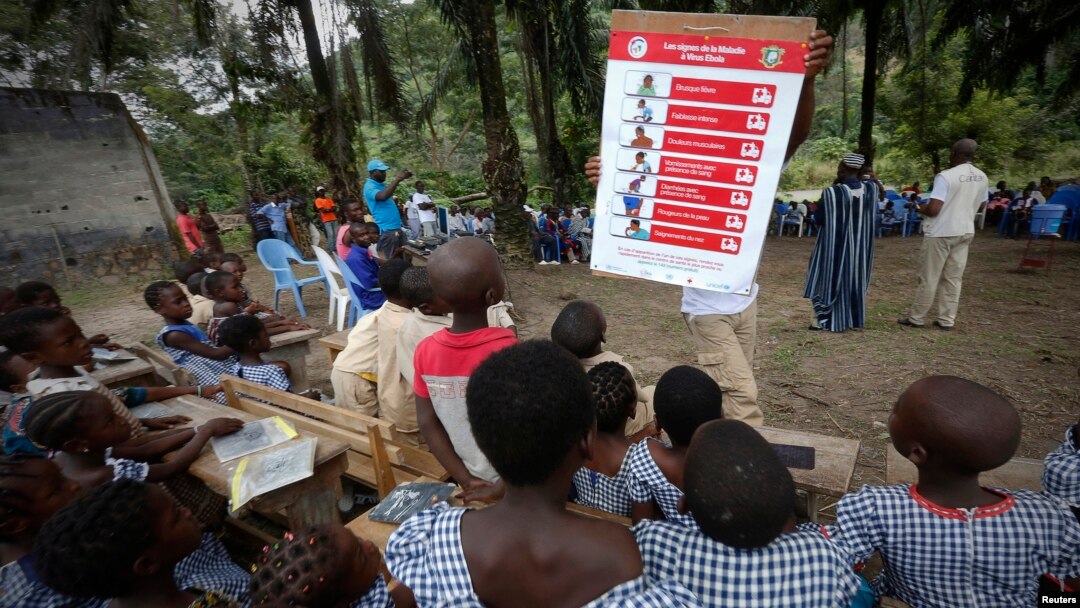 A man shows students a poster on the symptoms of Ebola during a United Nations Children's Fund (UNICEF) Ebola awareness drive in Gueupleu, Man, western Ivory Coast, Nov. 3, 2014. 