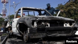 An Afghan policeman inspects the wreckage of a car after a Taliban attack on a guesthouse in Kabul, May 27, 2015.