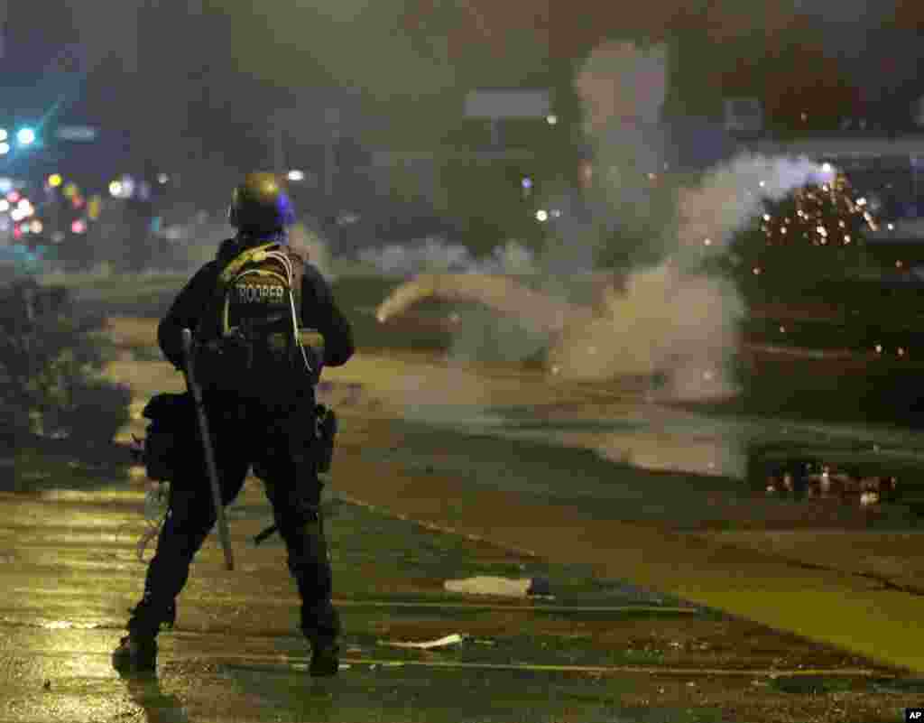 A law enforcement officer watches, Aug. 17, 2014, as tear gas is fired to disperse a crowd protesting the shooting of teenager Michael Brown last Saturday in Ferguson.