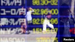 A man holding a mobile phone is reflected in an electronic board displaying foreign currency rates against the Japanese yen and market indices from around the world outside a brokerage in Tokyo, Oct. 11, 2013. 