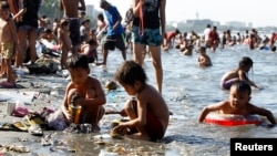 Children play with sand among garbage washed ashore as their family bathe in the waters of the Manila Bay during Easter Sunday in Manila, Mar. 31, 2013. 