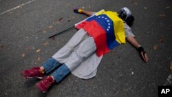 Un manifestante cubierto con la bandera venezolana yace en el suelo durante una protesta contra la violencia en Caracas.