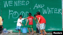 Children help to carry pails of drinking water as they walk past graffiti calling for help after Typhoon Haiyan devastated Tacloban city, central Philippines, Nov. 12, 2013.