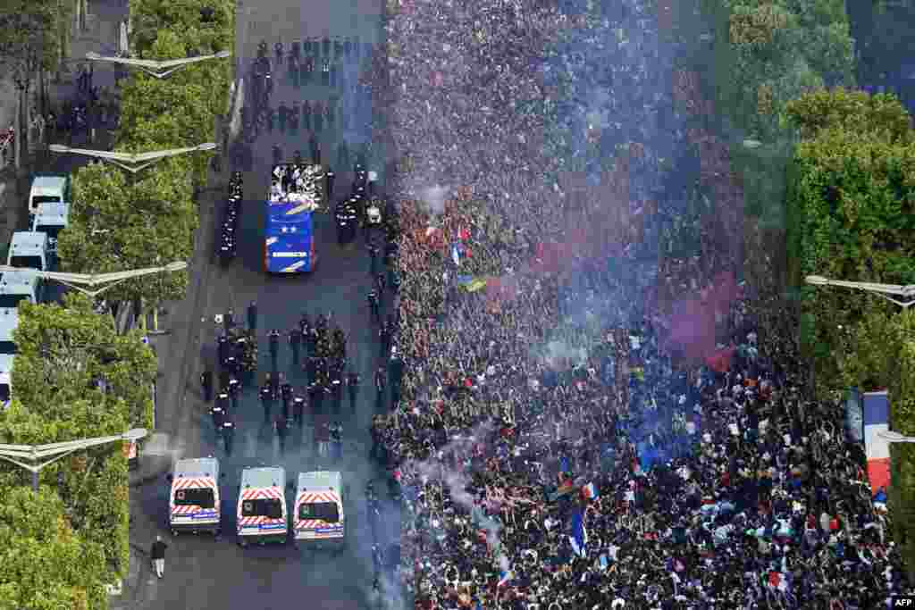 Para pendukung timnas Perancis menyambut para pemain Perancis yang berada di atap bus saat perayaan sebagai juara Piala Dunia 2018 dalam parade di sepanjang Champs-Elysee avenue di Paris.