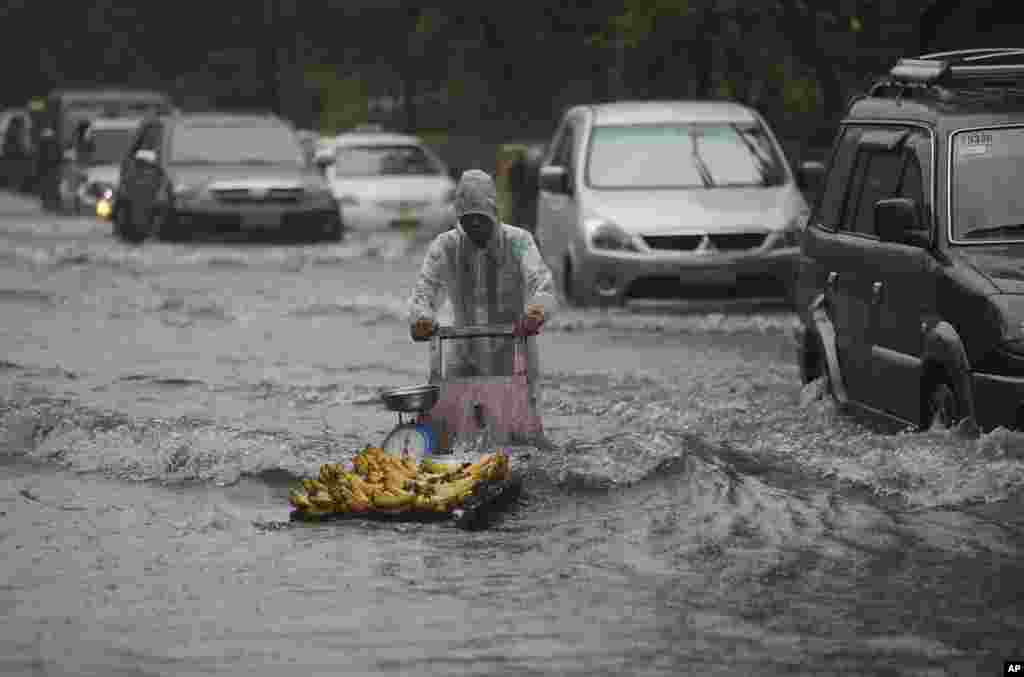 Penjual pisang menyeberangi jalan yang kebanjiran akibat hujan monsoon yang diperburuk oleh Topan Usagi di Manila, Filipina (22/9). (AP/Aaron Favila)