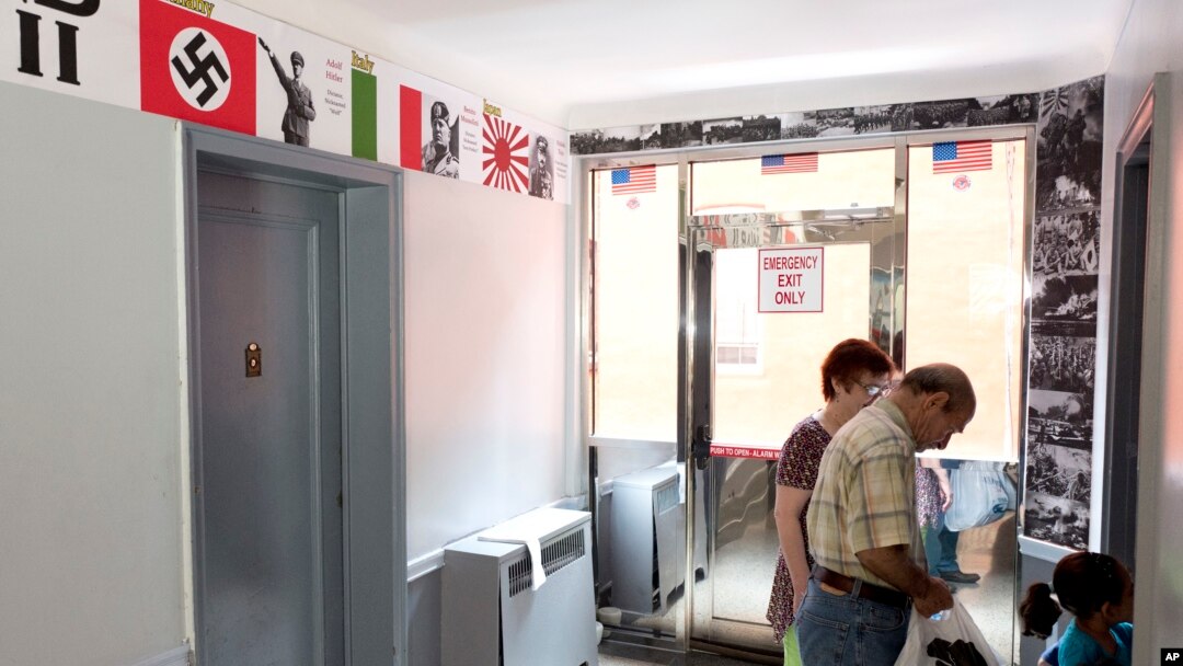 FILE - Residents of an apartment building pass posters of Adolf Hitler and Benito Mussolini in the hallway as they enter an apartment, Aug. 23, 2017, in the Queens borough of New York. New York City Councilman Jimmy Van Bramer protested the display of anti-semitic posters in the building. 