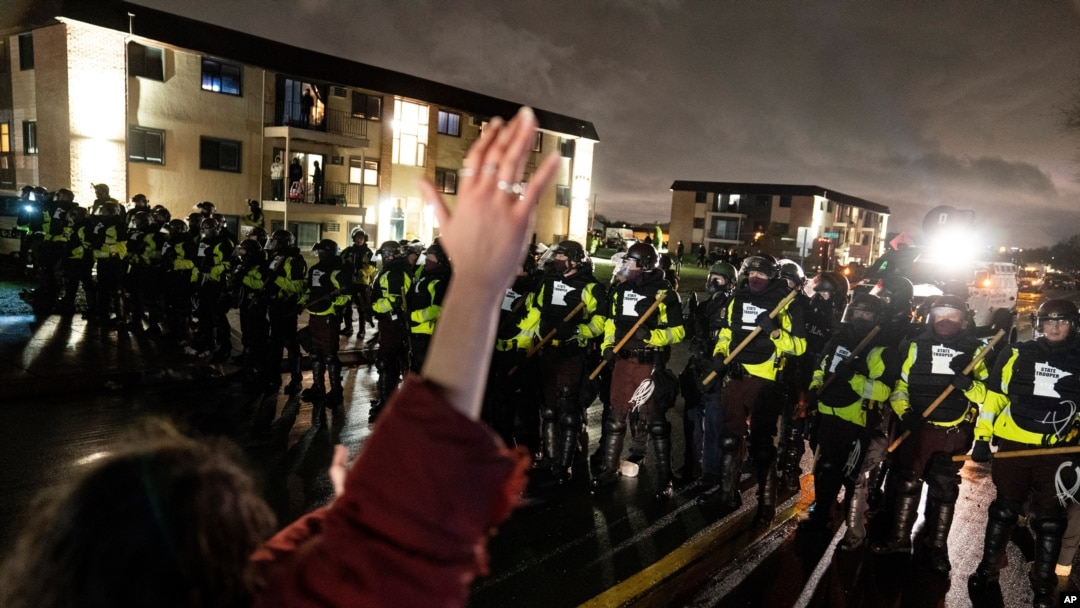 A demonstrator raises their hand while facing off against a perimeter of police as they defy an order to disperse during a protest against the police shooting of Daunte Wright, April 12, 2021, in Brooklyn Center, Minn.