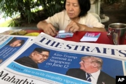 A news vendor counts her money near a stack of newspapers with a photo of U.S. President Donald Trump, right, and North Korea's leader Kim Jong Un on its front page on May 11, 2018, in Singapore.