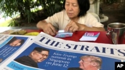 A news vendor counts her money near a stack of newspapers with a photo of U.S. President Donald Trump, right, and North Korea's leader Kim Jong Un on its front page in Singapore, May 11, 2018. 