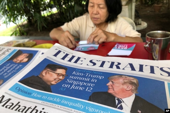 A news vendor counts her money near a stack of newspapers with a photo of U.S. President Donald Trump, right, and North Korea's leader Kim Jong Un on its front page on May 11, 2018, in Singapore.