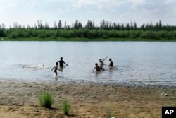 In this handout photo taken Sunday, June 21, 2020 and provided by Olga Burtseva, children play in the Krugloe lake outside Verkhoyansk, the Sakha Republic, about 4660 kilometers northeast of Moscow, Russia. (Olga Burtseva via AP)
