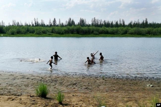 In this handout photo taken Sunday, June 21, 2020 and provided by Olga Burtseva, children play in the Krugloe lake outside Verkhoyansk, the Sakha Republic, about 4660 kilometers northeast of Moscow, Russia. (Olga Burtseva via AP)