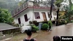 Orang-orang menyaksikan sebuah rumah yang hanyut terbawa arus sungai setelah hujan lebat melanda wilayah Kottayam, Kerala, India, pada 17 Oktober 2021. (Foto: Reuters TV/ANI/Kerala Government Public Relations Office/Handout via Reuters)