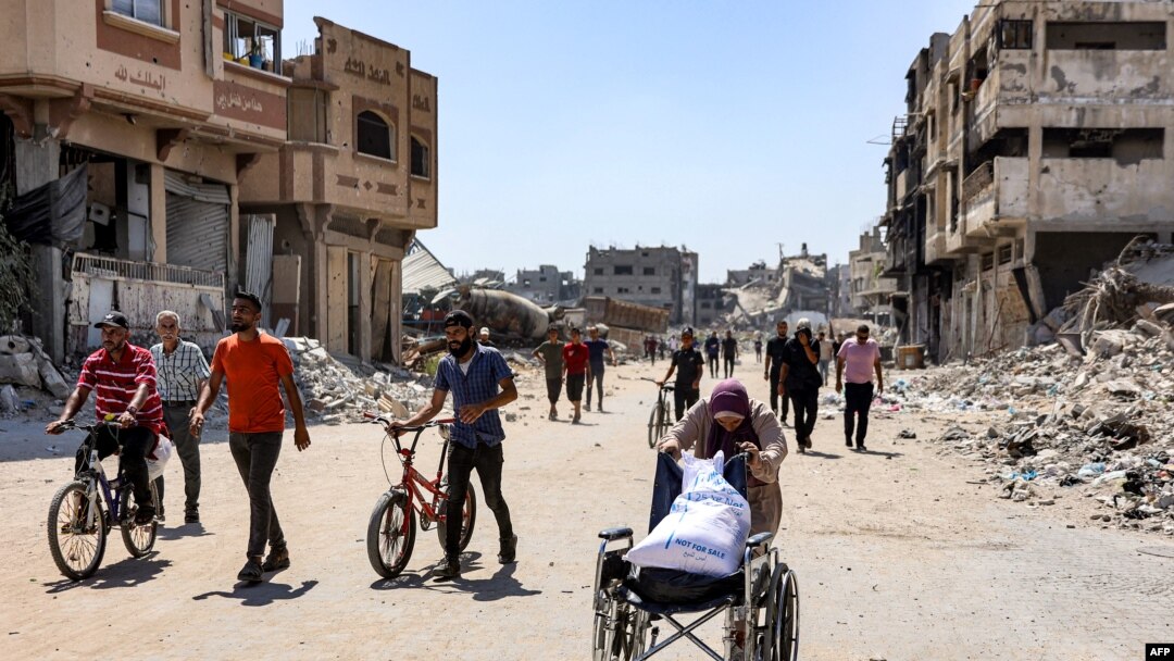 8 Temmuz 2024 - Gazze kent merkezinde yaşlı bir kadın, tekerlekli sandalyeye koyduğu un çuvalını taşıyor.