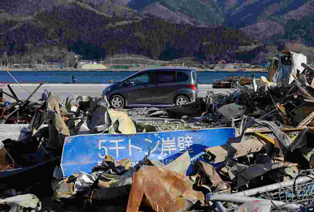 A car passes in front of tsunami debris piled up on the wharf in Ofunato, Iwate Prefecture nearly one year after the March 11 tsunami devastated the area, January 15, 2012 (AFP)