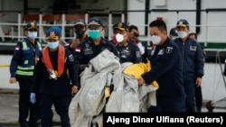 Anggota penyelamat membawa sisa-sisa pesawat Sriwijaya Air penerbangan SJ182 yang jatuh ke laut, di pelabuhan Terminal Kontainer Internasional Jakarta, 10 Januari 2021. (Foto: REUTERS/Ajeng Dinar Ulfiana)