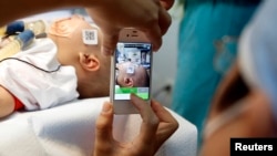 FILE - A doctor uses a smartphone to take a photo of a child with facial deformity before surgery at the Vietnam Cuba hospital in Hanoi, Vietnam Nov. 18, 2014. (Reuters/Kham)