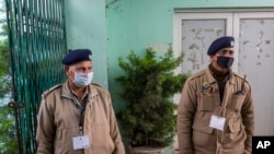 FILE - Indian police officials wear protective masks as they stand guard at an entrance of Himachal Pradesh Cricket Association.
