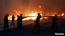 Para petugas pemadam kebakaran, tentara dan masyarakat setempat memanggul selang air sementara kebakaran hutan membakar Kota Rafina, dekat Athena, Yunani, 23 Juli 2018.
