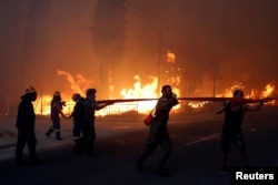 Bomberos, soldados y residentes locales llevan una manguera mientras un incendio forestal arde en la ciudad de Rafina, cerca de Atenas, Grecia, el 23 de julio de 2018.